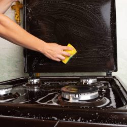 cleaning the kitchen, surface cleaning on the gas stove, washing the stove with a yellow washcloth, household kitchen appliances.